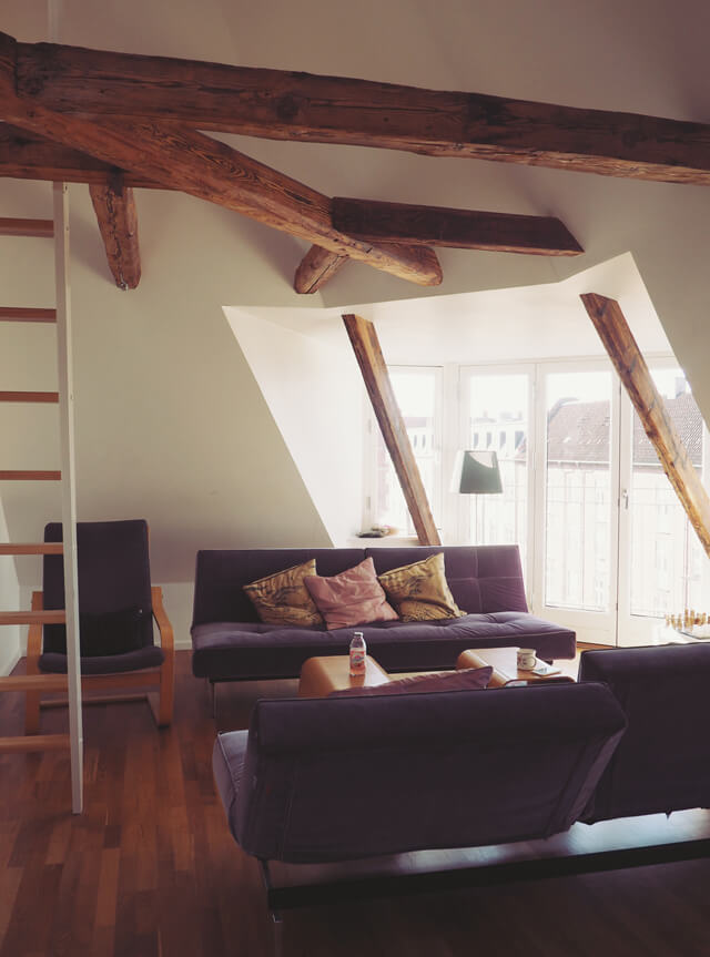 Apartment in Copenhagen with white walls and ceiling, and exposed beams. Two grey sofas and a ladder.