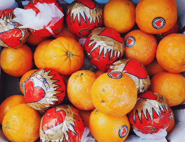 A box of oranges, some are wrapped in a red and gold heart print paper