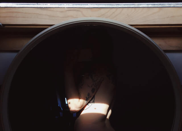 A mirror selfie of Lyzi's nude body in the shadows, with a band of light across her elbow and torso