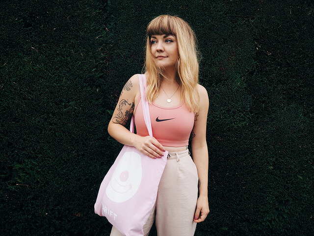 Lyzi wears a pink sports bra, neutral trousers and shoes, and pink Drift tote bag