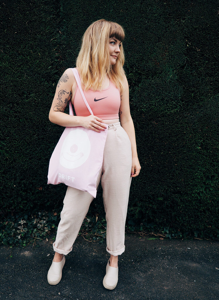 Lyzi wears a pink sports bra, neutral trousers and shoes, and pink Drift tote bag