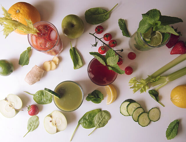 colourful flatlay of fruit and vegetables with 4 glasses of healthy juices and boozy cocktails