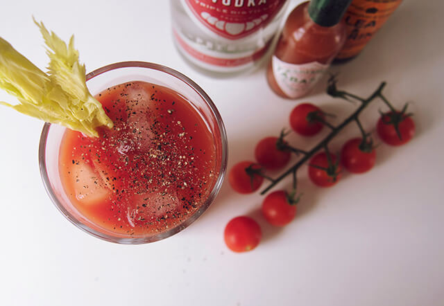 colourful flatlay of tomatoes, tabasco and vodka with a glass of Bloody Mary