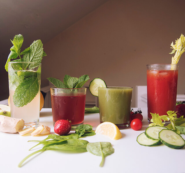 display of fruit and vegetables with 4 glasses of healthy juices and boozy cocktails