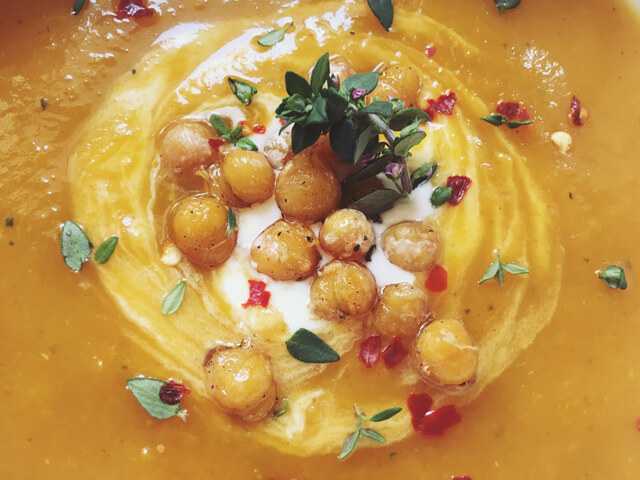 A close up of butternut squash soup with crispy chickpeas, thyme and chilli flakes