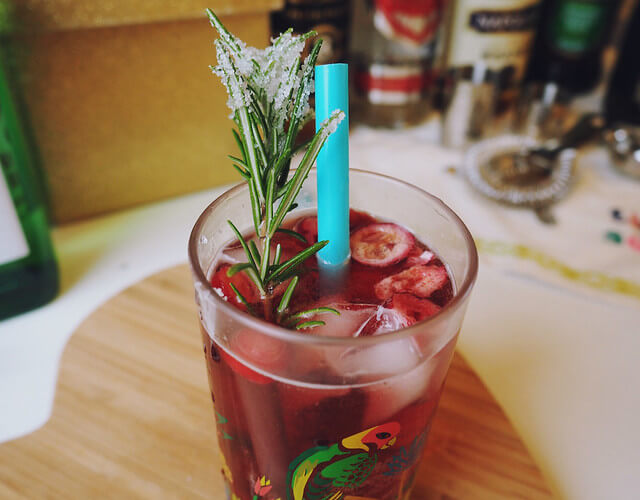 Close up of Cranberry Mule cocktail with a blue straw and rosemary garnish