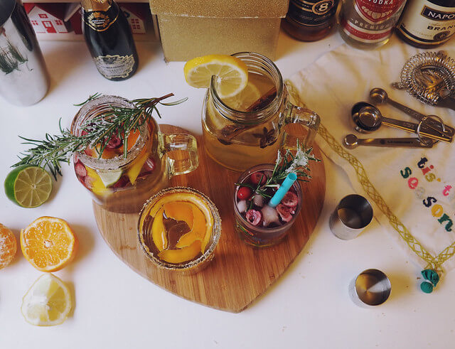 Four colourful Christmas cocktails from above on a wooden board with Christmas decorations and bottles of booze in the background