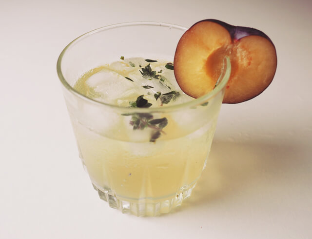 Glass of Prosecco Thyme cocktail from the side, with a thyme and a plum slice garnish