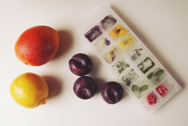 Flat lay of fruit and Ice cubes with flowers and herbs and raspberries