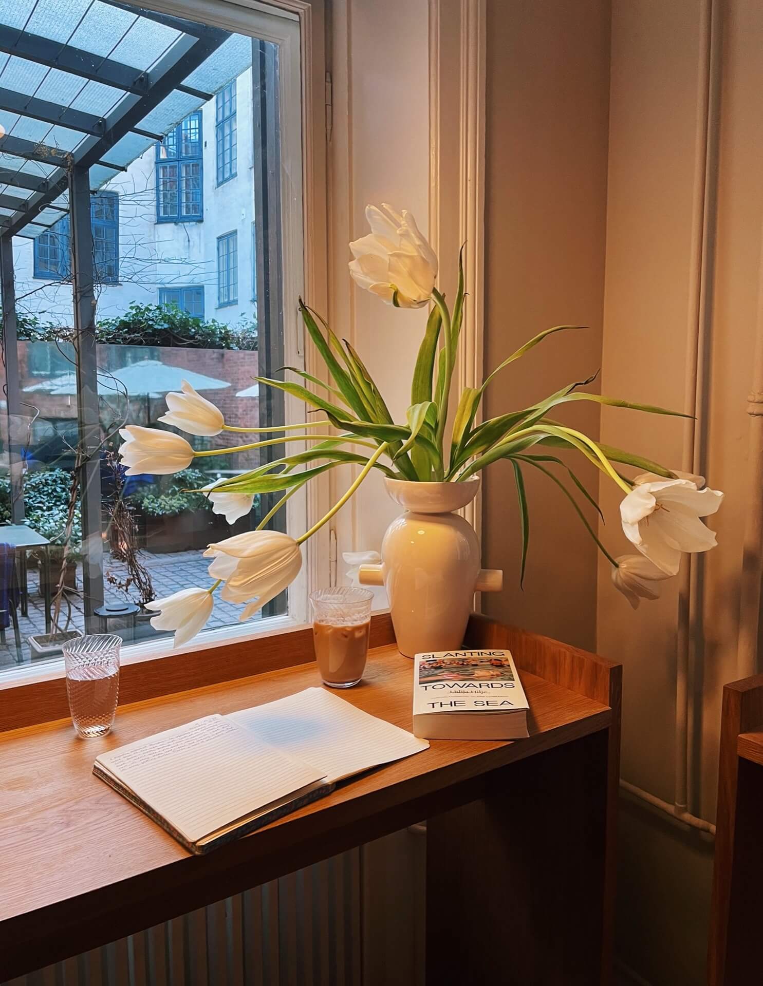 Large white tulips next to a coffee, book and notebook