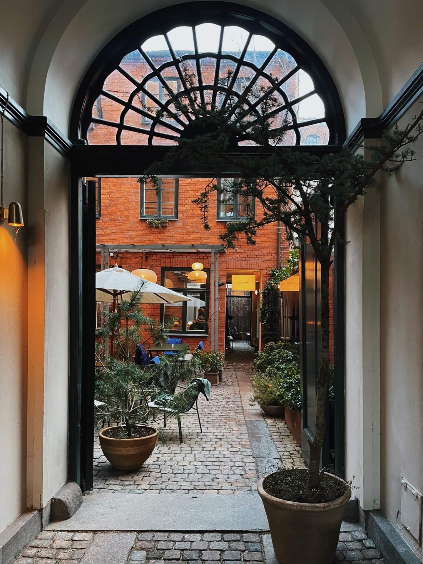 Arched doorway into Lille Petra courtyard with tables, parasols and cosy lighting. 